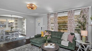 A living room with a green sofa, a coffee table, and a dining area with a table and chairs. - The Duke | 3BR 1 BA | Pet Friendly! (Columbia)