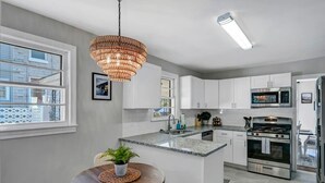 A modern kitchen with white cabinets, a stainless steel stove, and a large island with a sink. - The Duke | 3BR 1 BA | Pet Friendly! (Columbia)