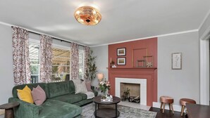 A living room with a green sofa, a fireplace, and a chandelier. - The Duke | 3BR 1 BA | Pet Friendly! (Columbia)