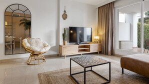 A modern living room with a television, a wicker chair, a coffee table, and a large window with curtains. - Casa Livia with Auping beds (Estepona)