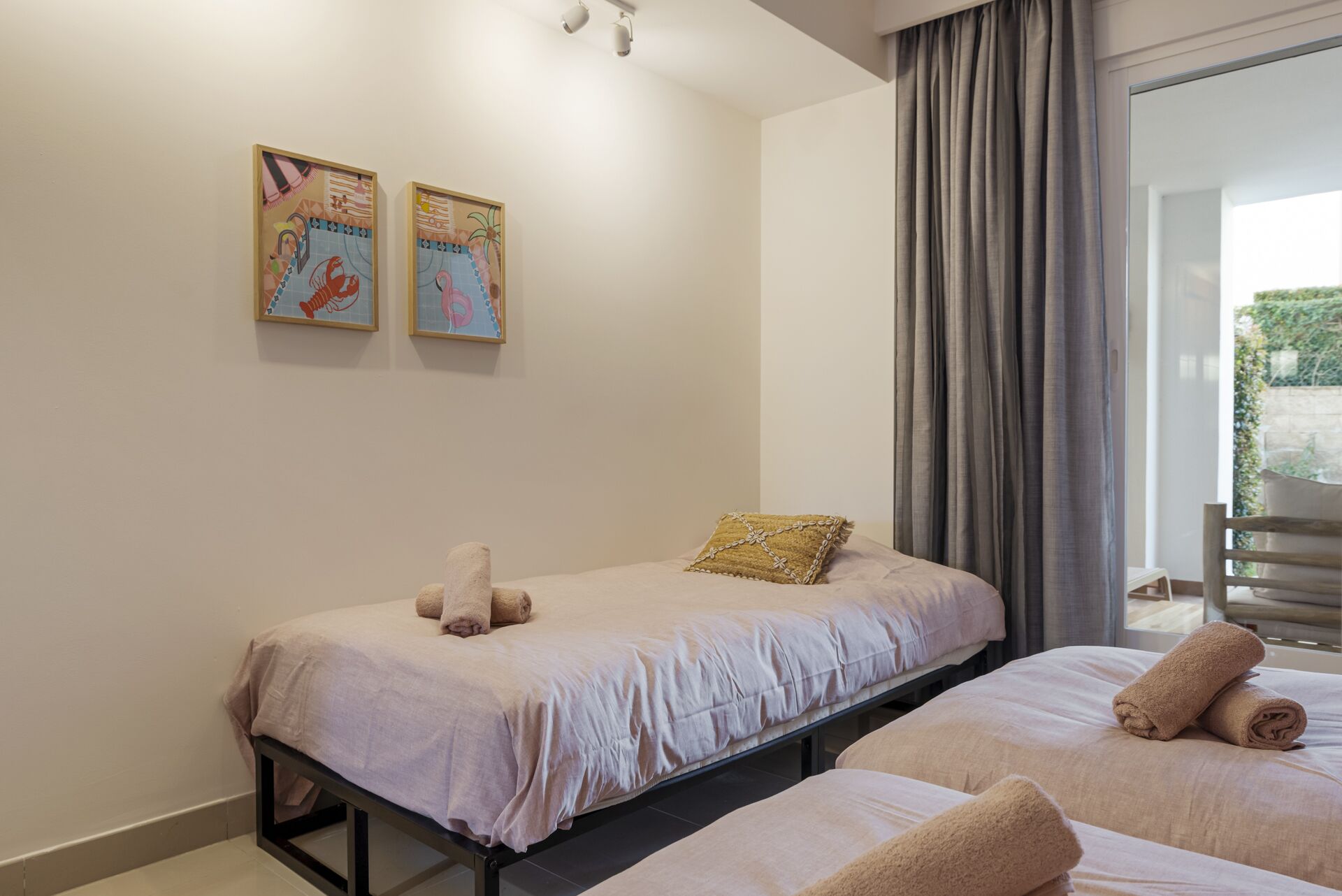 A bedroom with two beds, a large window with curtains, and two wall-mounted artworks.