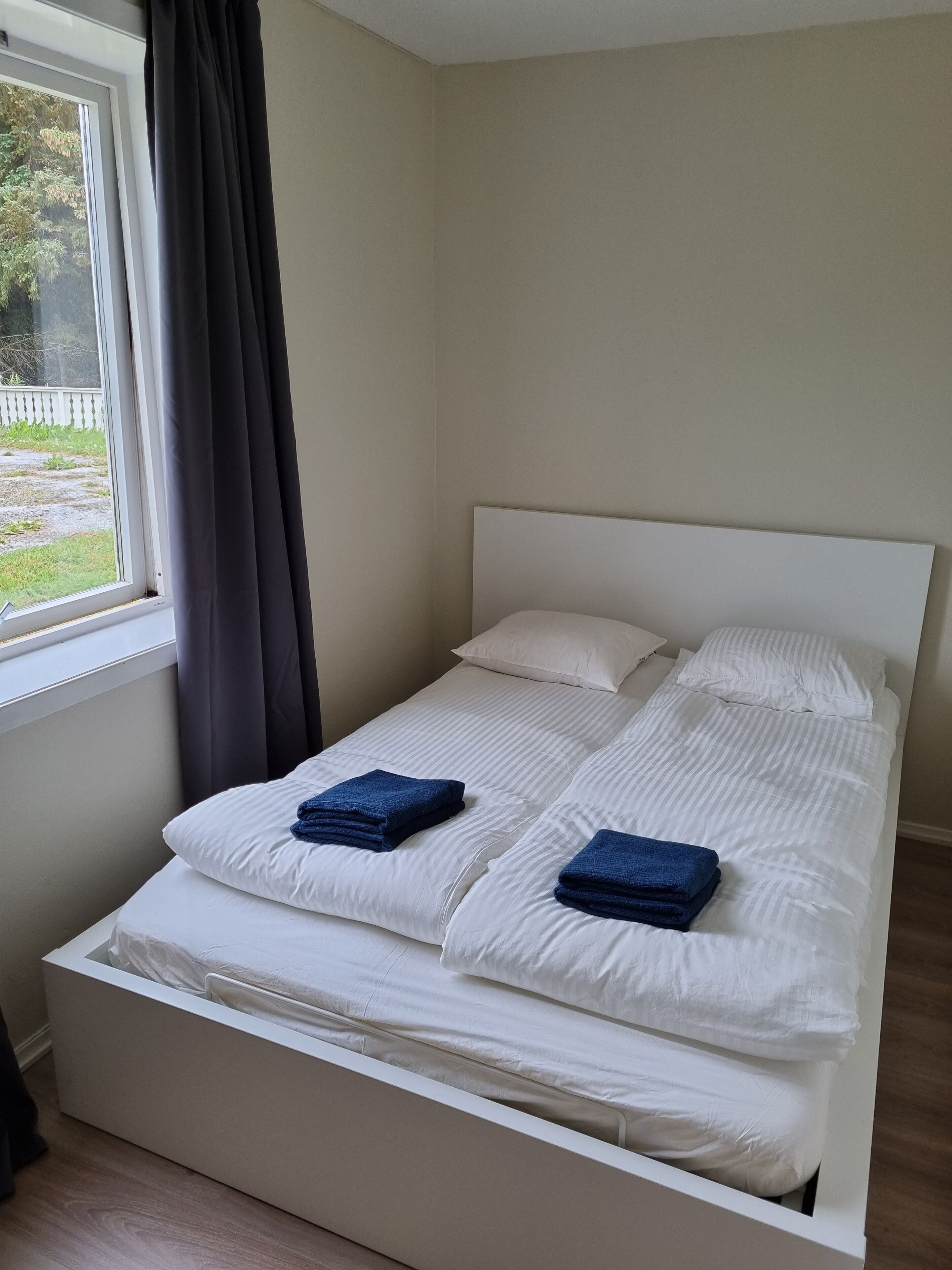 A neatly made bed with white bedding and two folded blue towels.