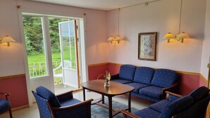 A room with a blue sofa, two armchairs, a small table, and a window with a view of greenery. - Vollvaagen Apartments Smøla (Smøla)