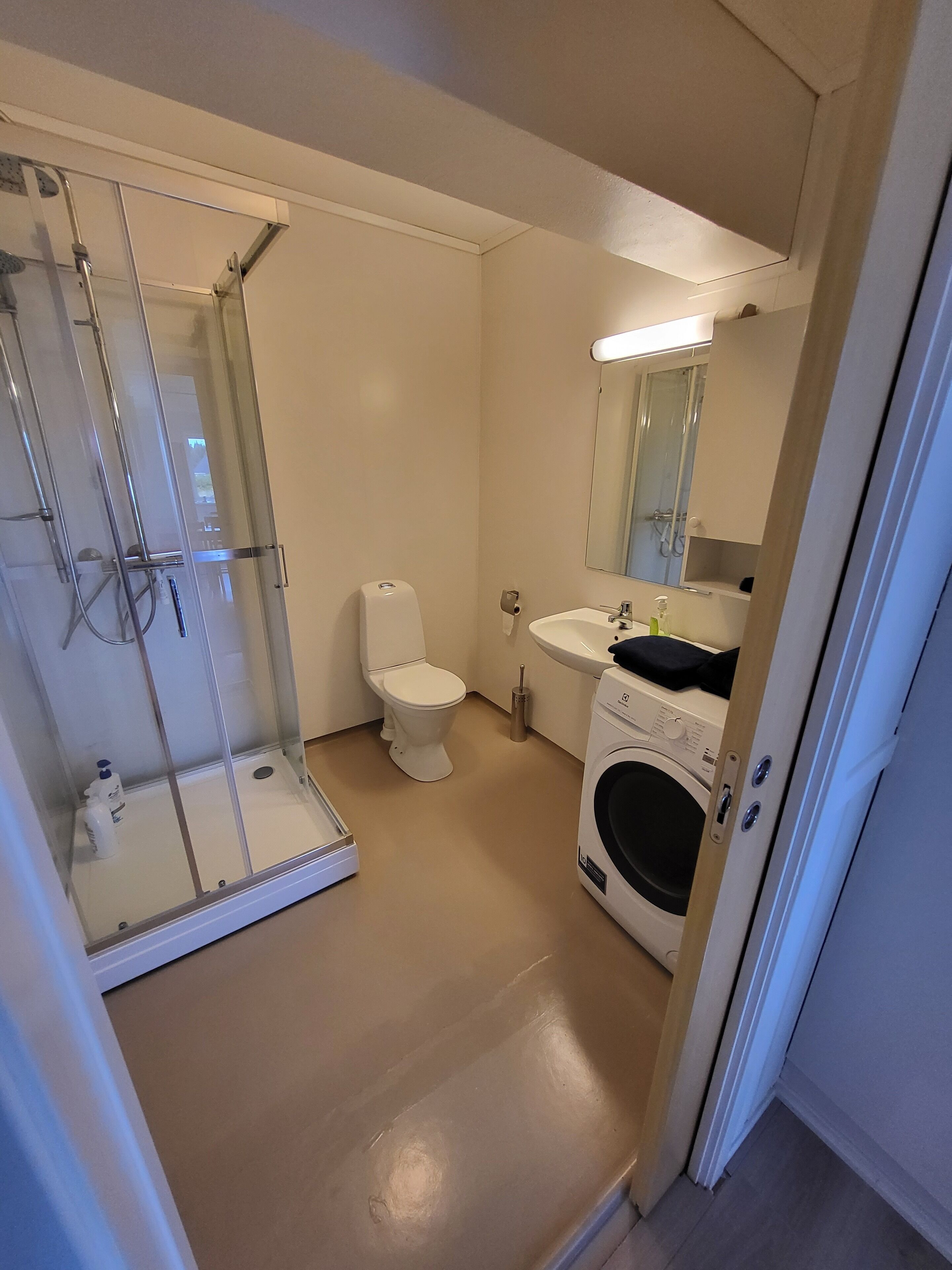 Un baño con ducha de vidrio, inodoro, lavamanos y lavadora.