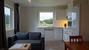 A compact living space with a sofa, a dining table, and a kitchen area including a refrigerator and stove. - Vollvaagen Apartments Smøla (Smøla)