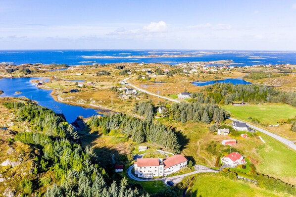 An aerial view of a coastal area with a large building surrounded by greenery and a body of water.