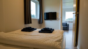 A hotel room with a bed, a TV mounted on the wall, and a view of the outside through a window. - Vollvaagen Apartments Smøla (Smøla)