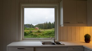 A kitchen with a window view of a green landscape and a house. - Vollvaagen Apartments Smøla (Smøla)