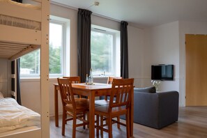A room with a bunk bed, a dining table with chairs, a grey sofa, and a TV mounted on the wall.