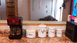 Un comptoir de cuisine avec une machine à café, quatre récipients étiquetés « filtres à café », « sucre » et « thé », et un four à micro-ondes.