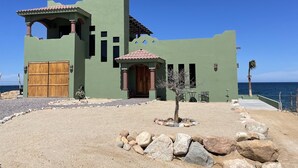 Un bâtiment à deux étages avec une façade verte, une porte en bois et un petit patio agrémenté de rochers et d’un arbre.
