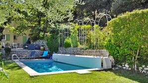Una piscina con pared de piedra y escalones, rodeada de vegetación y una pérgola.