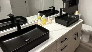 Une salle de bain moderne avec un grand miroir, deux lavabos noirs et un meuble-lavabo blanc doté de tiroirs.