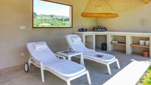 Une pièce avec deux chaises longues blanches, une petite table avec une radio et une vue sur la verdure par une fenêtre.