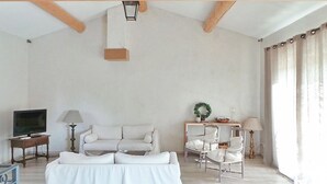 Un salon spacieux avec un canapé blanc, une petite table avec une lampe, un téléviseur et une couronne décorative posée sur une table d’appoint.