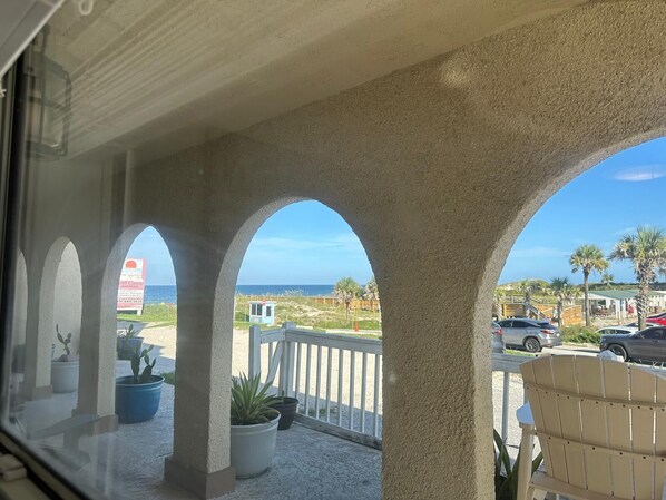 A covered outdoor area with three arches, potted plants, and a view of the beach and ocean.