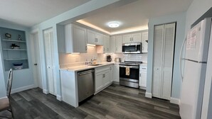 A modern kitchen with white cabinets, stainless steel appliances, and a wooden floor. - Crescent Beach Retreat - Steps to Sand - Pet Friendly (St. Augustine)