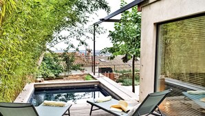 A rooftop pool area with two lounge chairs, a small hot tub, and a view of the cityscape.