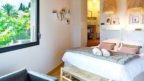 A bedroom with a bed, a bench, a window, and a view of greenery outside.