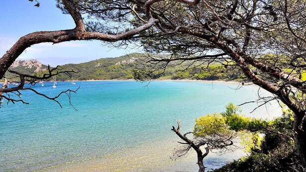 A coastal landscape with clear turquoise waters, a sandy beach, and a backdrop of hills.