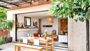 An open-plan living and dining area with a wooden table and benches, a hanging light fixture, and a variety of potted plants.