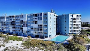 Un hôtel moderne à plusieurs étages, doté d’une piscine, entouré de verdure et offrant une vue sur un ciel dégagé.