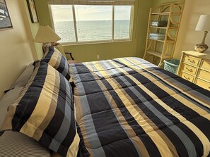 A bedroom with a large bed, a window with a view of the sea, a wooden ladder, and a dresser with drawers. - Oceanfront Penthouse Paradise Condo on Anna Maria Island! (Holmes Beach)