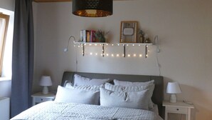 Una camera da letto con un letto, comodini, una lampada a sospensione e una mensola con oggetti decorativi.