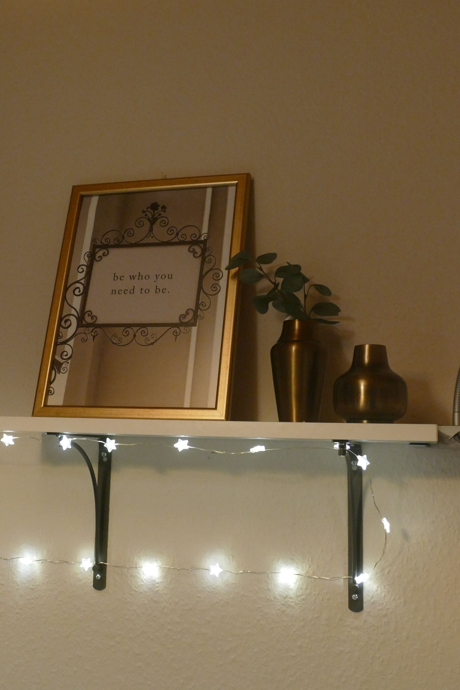 Ein gerahmtes Zitat an einer Wand, ein Blumentopf und eine Lichterkette.