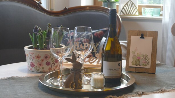 Un vassoio con una bottiglia di vino, due bicchieri, una piccola candela e una pianta in vaso su un tavolo.