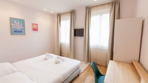 Habitación de hotel con cama, escritorio, silla, televisor y dos cuadros colgados en la pared.