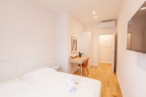 Une chambre à coucher comprenant un lit, un bureau, une chaise, une petite table ronde et une porte donnant sur une autre pièce.