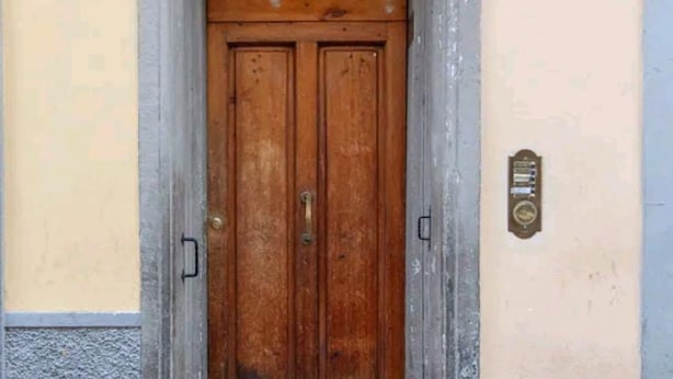 Una puerta doble de madera con un picaporte de latón, una placa de metal en la pared y una placa con un número sobre la puerta.