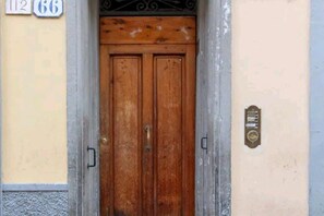 Une porte à deux battants en bois, dotée d’une poignée en laiton, une plaque métallique fixée au mur et une plaque numérotée au-dessus de la porte.