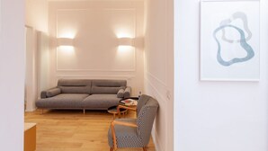 Una sala moderna con un sofá, un sillón estampado, una mesita y una obra de arte abstracto colgada en la pared.