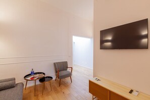 Une chambre moderne équipée d’un téléviseur à écran plat, d’un canapé, d’un fauteuil, d’une petite table ronde avec un magazine et d’un meuble en bois.