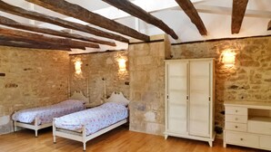 A rustic bedroom with two single beds, stone walls, wooden beams, and a white wardrobe.