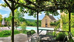 A covered outdoor seating area with a pool and stone building in the background.