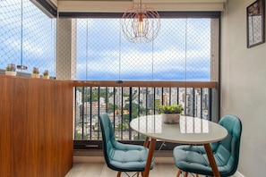 A balcony with a round table and two chairs, a hanging light fixture, and a view of the cityscape.