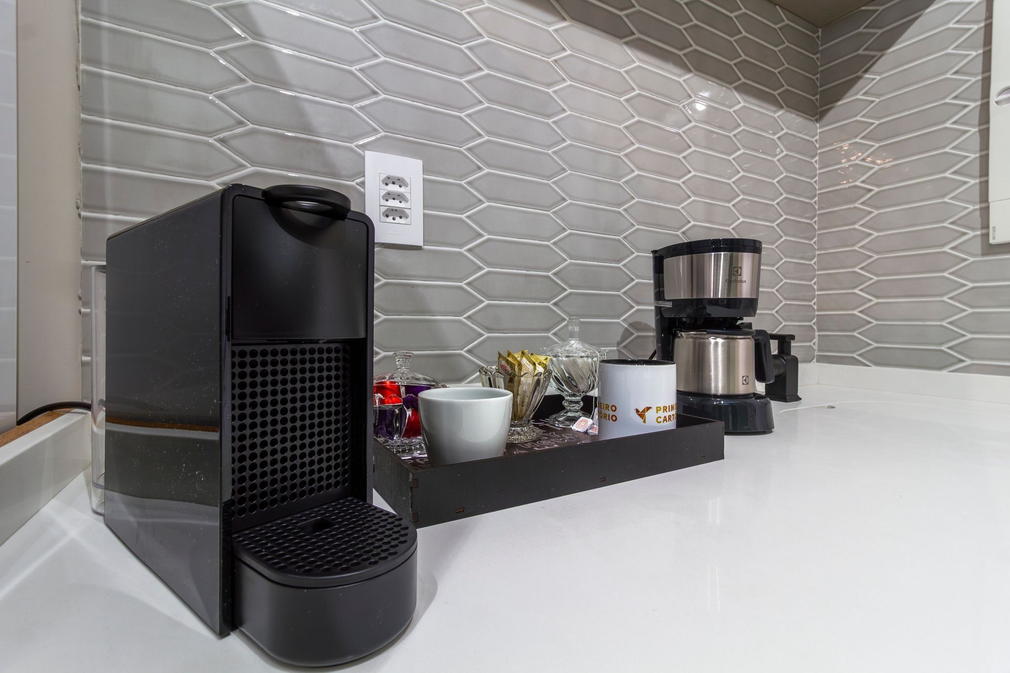 A kitchen with a coffee maker, a kettle, and a coffee station with cups and a vase.
