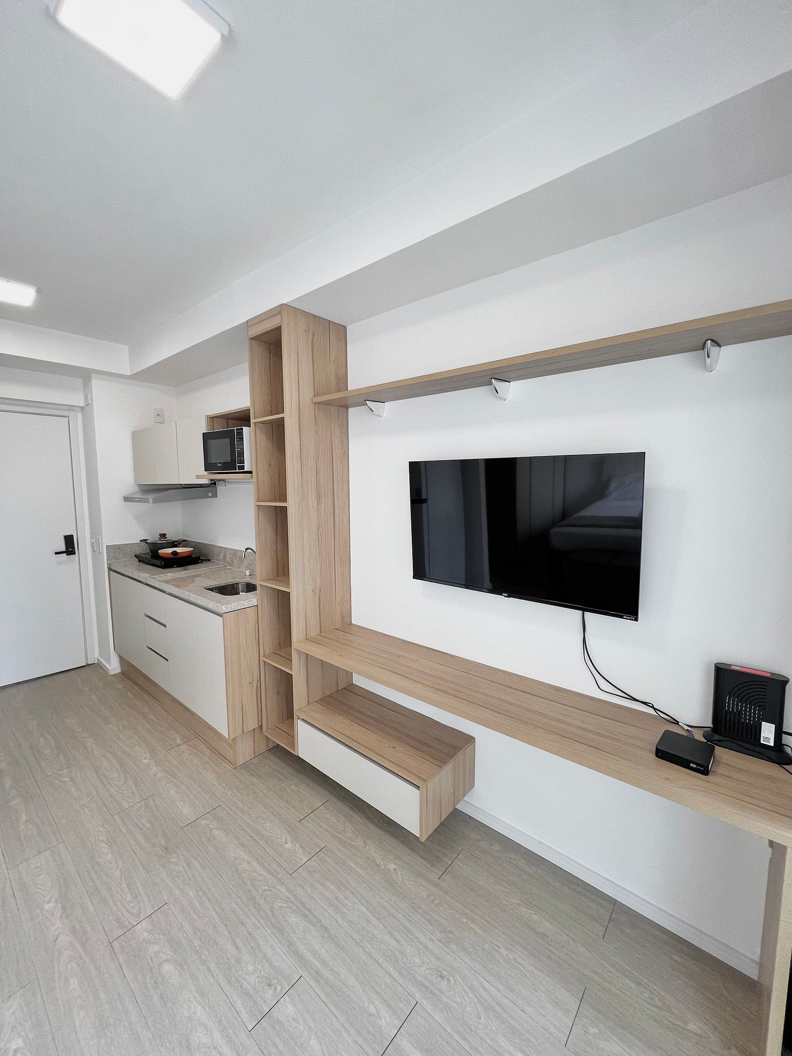A modern kitchen with built-in appliances, a TV mounted on the wall, and a wooden shelf unit.