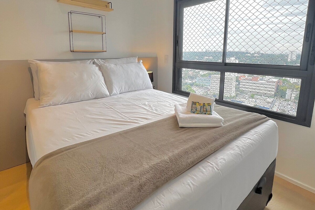 Een moderne slaapkamer met een groot bed, een raam met uitzicht en een houten plank boven het bed.