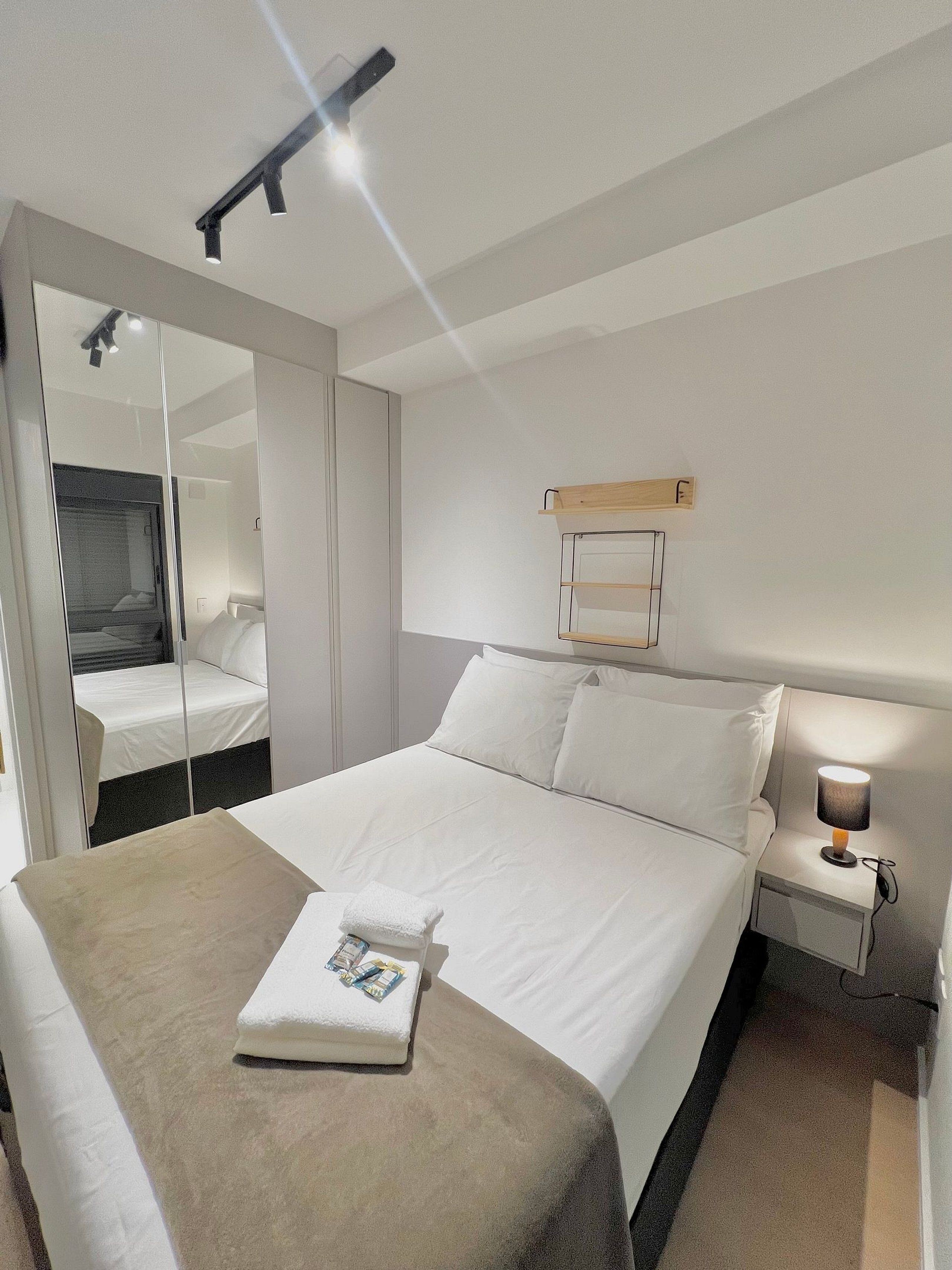 Une chambre d’hôtel avec un grand lit, une table de chevet avec une lampe, un miroir et une armoire.