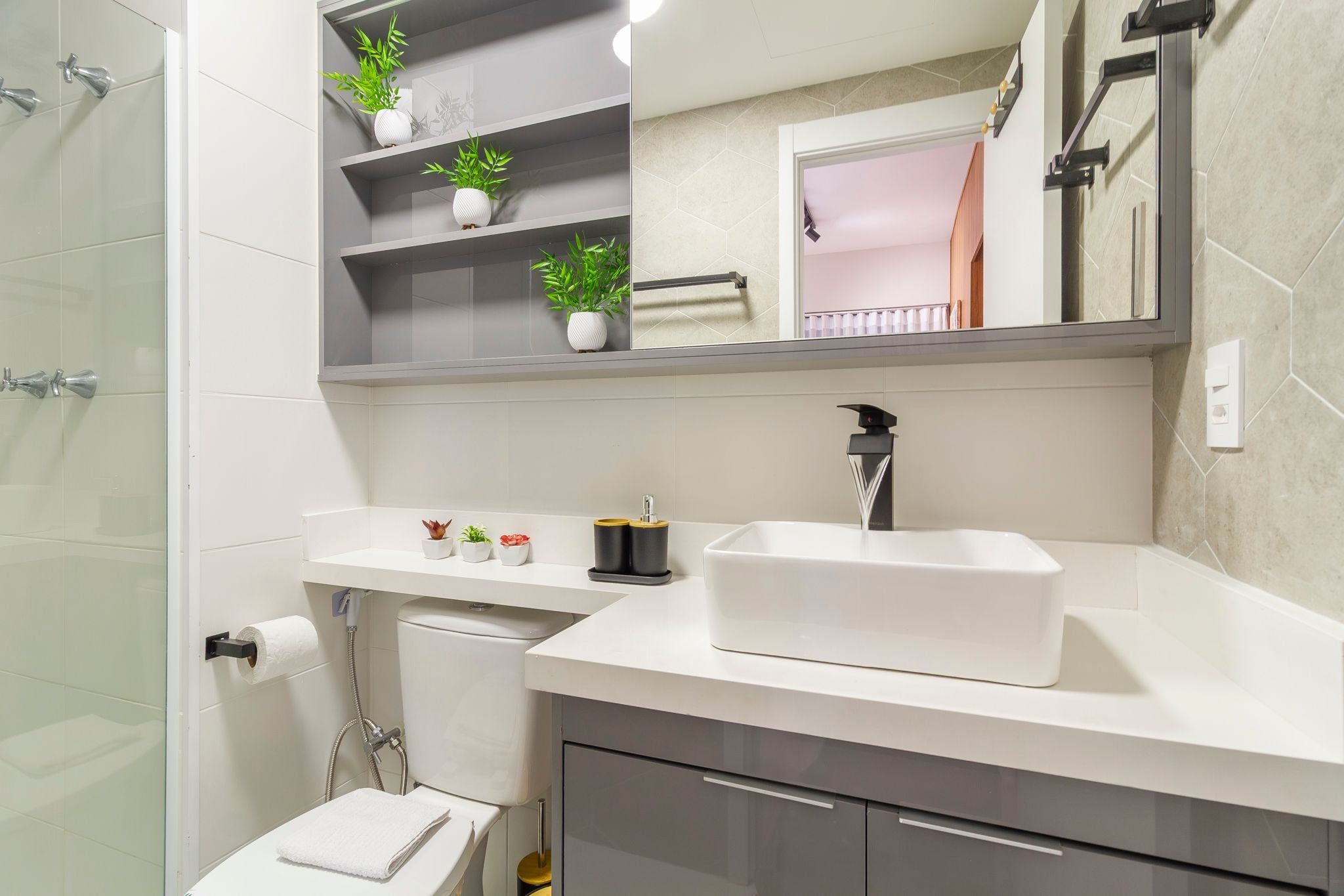 A modern bathroom with a glass shower enclosure, a white sink with a black faucet, and shelves with potted plants.