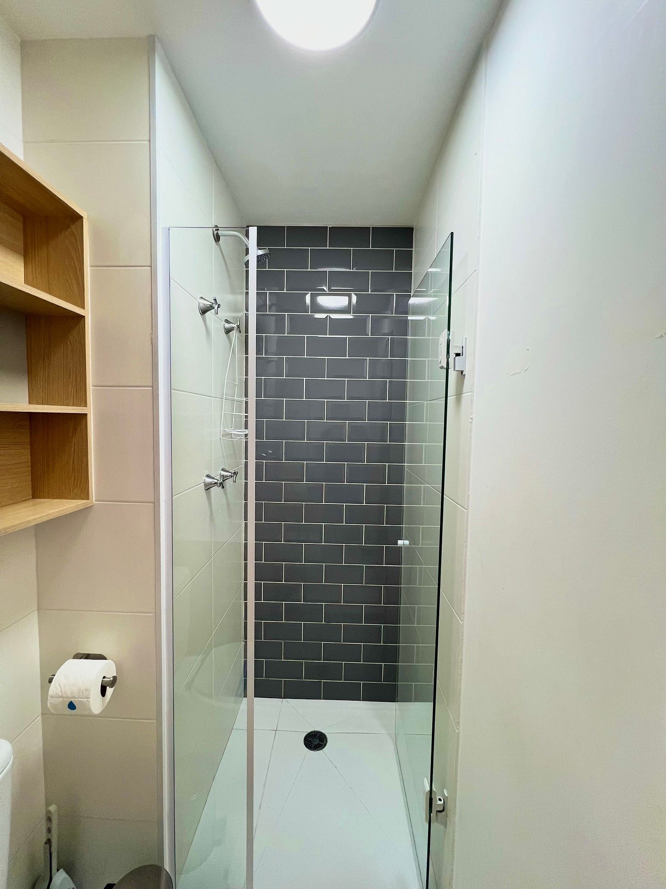 Ein modernes Badezimmer mit einer gläsernen Duschkabine, weißen Fliesen und einer Wand mit schwarzen Fliesen als Blickfang.