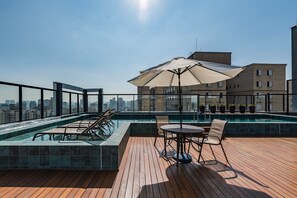 Un espace piscine aménagé sur le toit, avec des chaises longues, une table et un parasol.