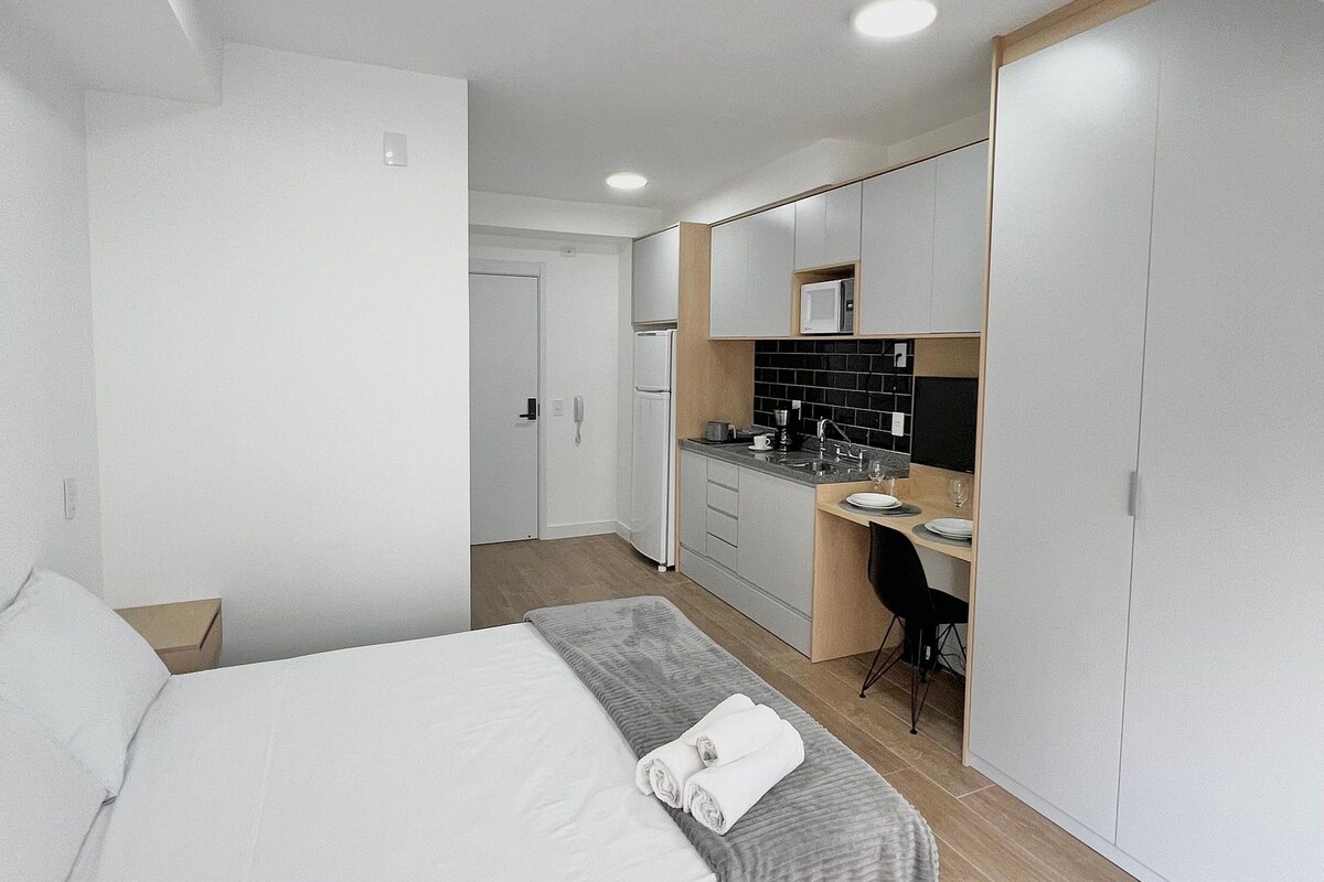 Une chambre d’hôtel moderne équipée d’un lit, d’un bureau, d’une kitchenette et d’une armoire.