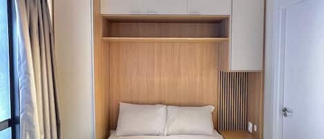 A hotel room with a bed, a bedside table, a wardrobe, and a window with curtains.