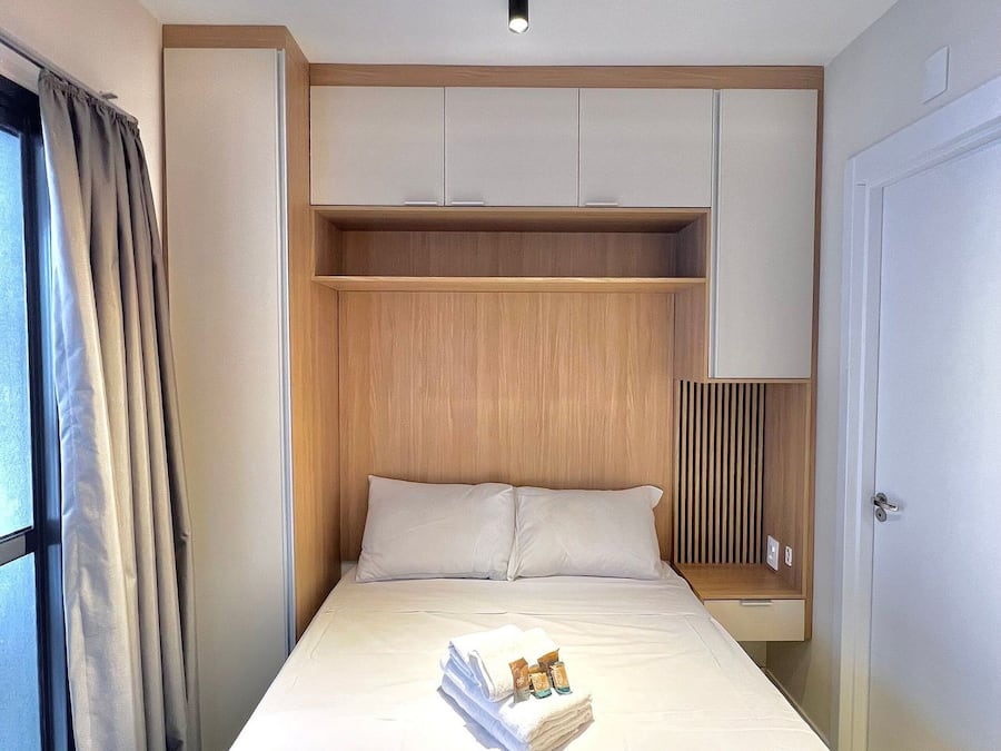 Een hotelkamer met een bed, nachtkastje, kast en een raam met gordijnen.