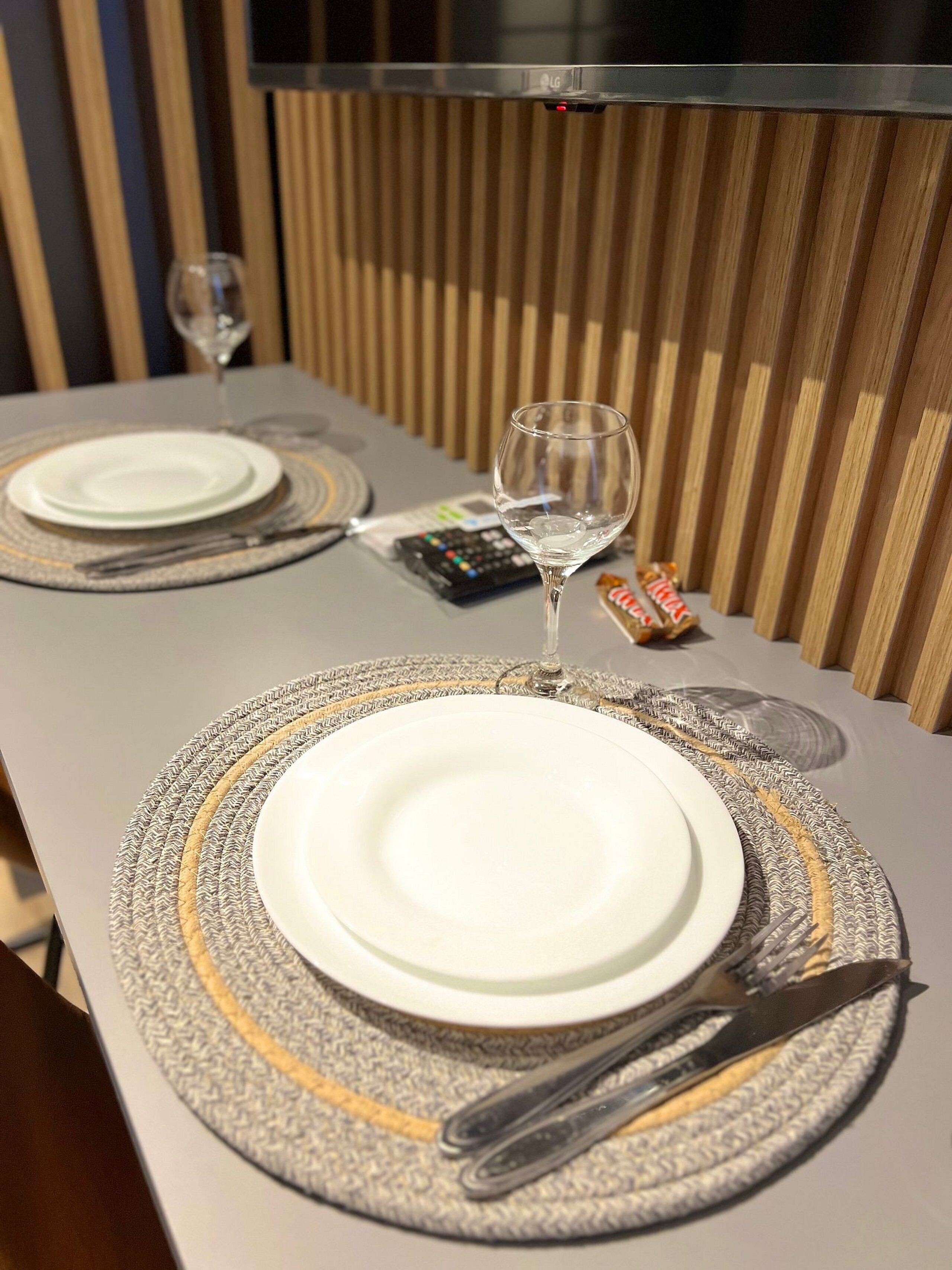 A table set with a white plate, a wine glass, cutlery, and a remote control.